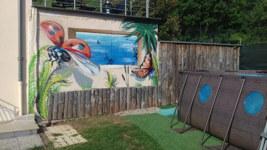 Mur de jardin peint d'une vue sur la mer avec une coccinelle et un papillon en trompe-l'œil