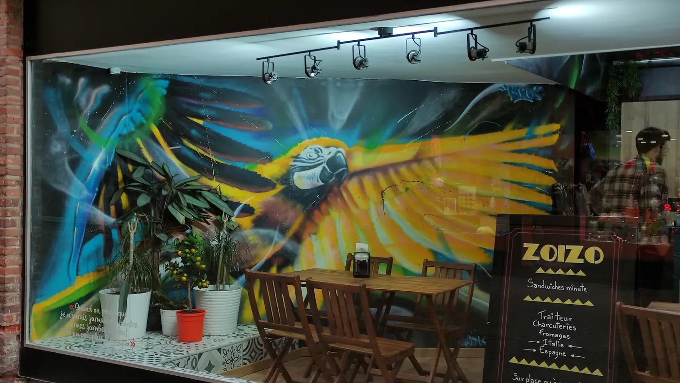 Vitrine du Zoizo peinte d'un grand perroquet aux ailes bleues et jaunes au milieu de feuillages